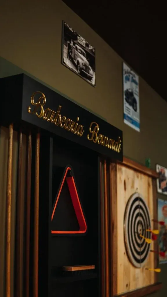 Letreiro dourado Barbearia Bernardi sobre o porta-tacos de sinuca